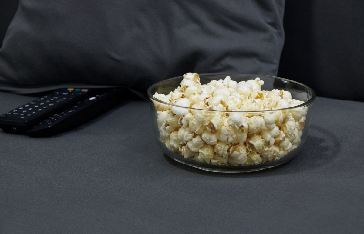 Popcorn bowl and remote controls on a sofa set up for a K-drama binge session