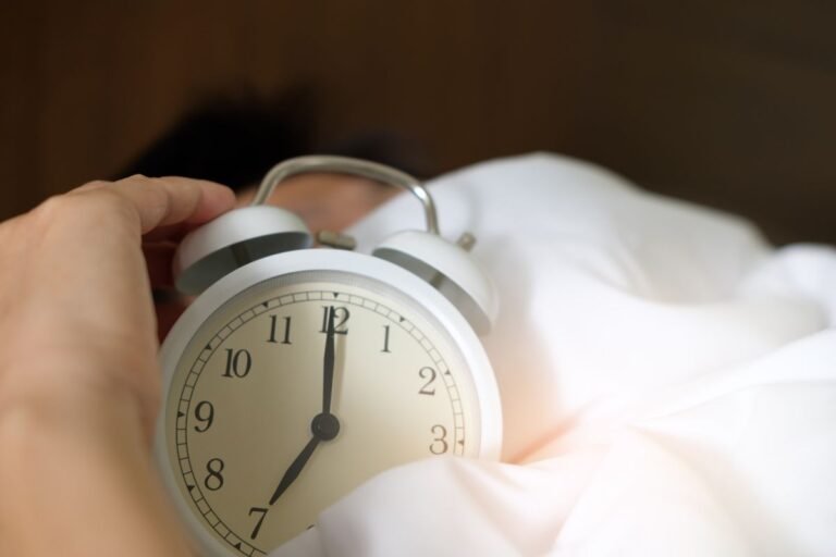 Hand reaching for an alarm clock while still in bed in the morning