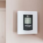 Smart thermostat mounted on a wall, used to compare climate-zone-specific models for 2026
