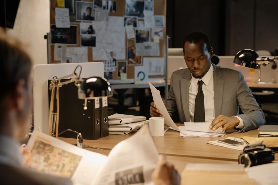 Detective examining documents at a dimly lit desk, representing the investigation storyline in A Bona Fide Killer