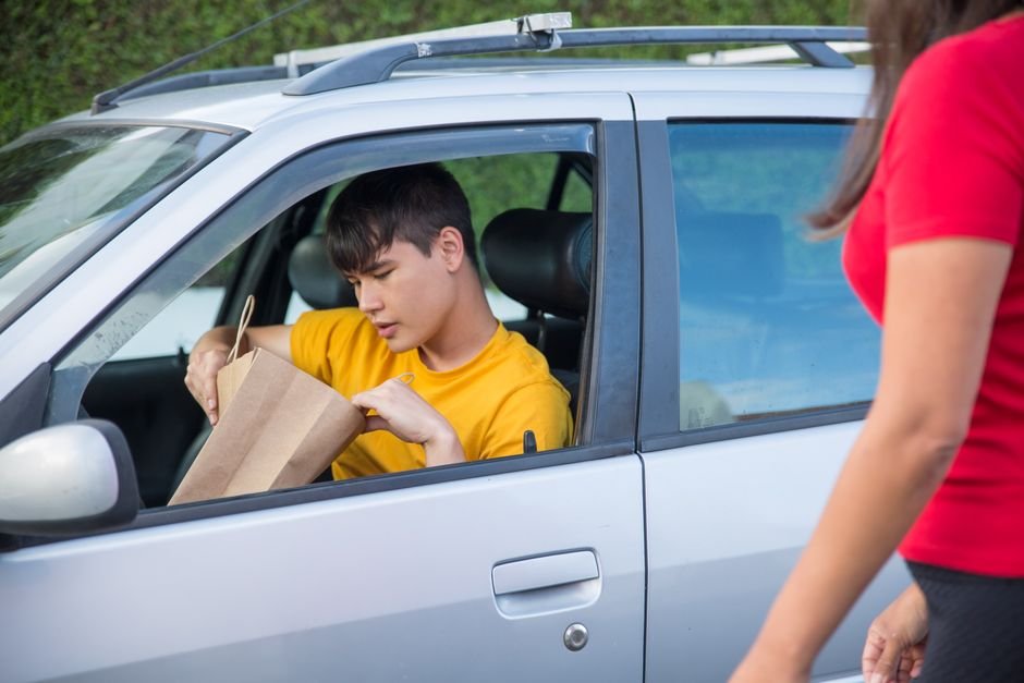 Delivery driver handing off a paper grocery bag order beside a car