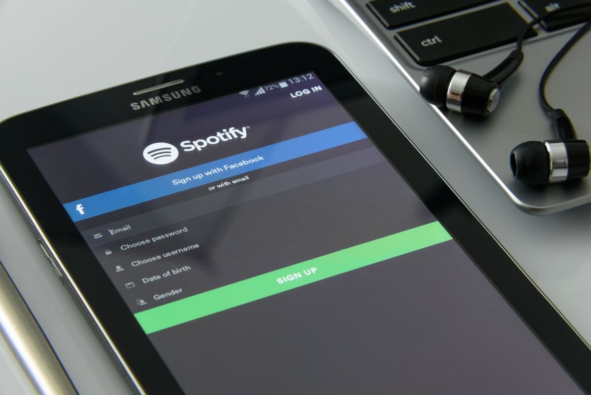 Smartphone showing a music streaming app next to a laptop and earphones, representing where to stream ENHYPEN THE SIN BLISS