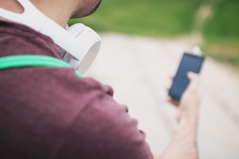 Person with headphones around their neck holding a smartphone, representing streaming a new album