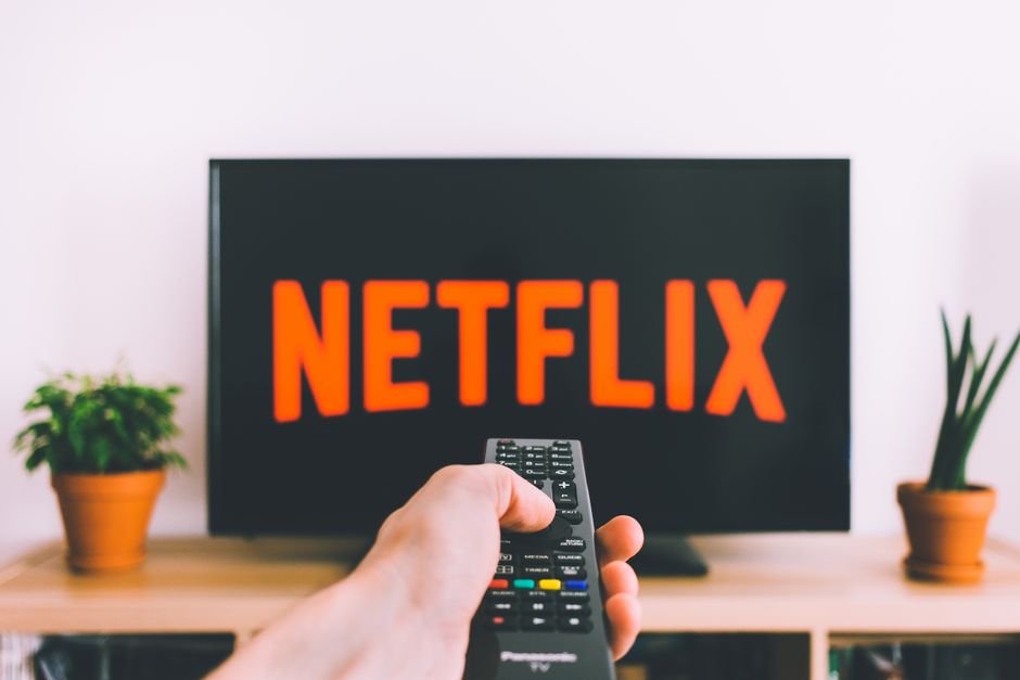 Hand holding a TV remote pointed at a Netflix streaming screen
