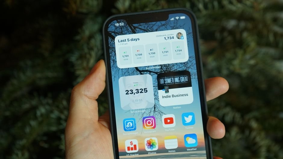 Hand holding a phone with app widgets, representing the Google Home app update that fixed broadcast