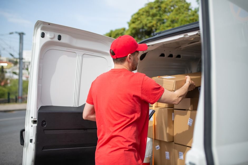 Delivery driver stacking package boxes at the back of a car
