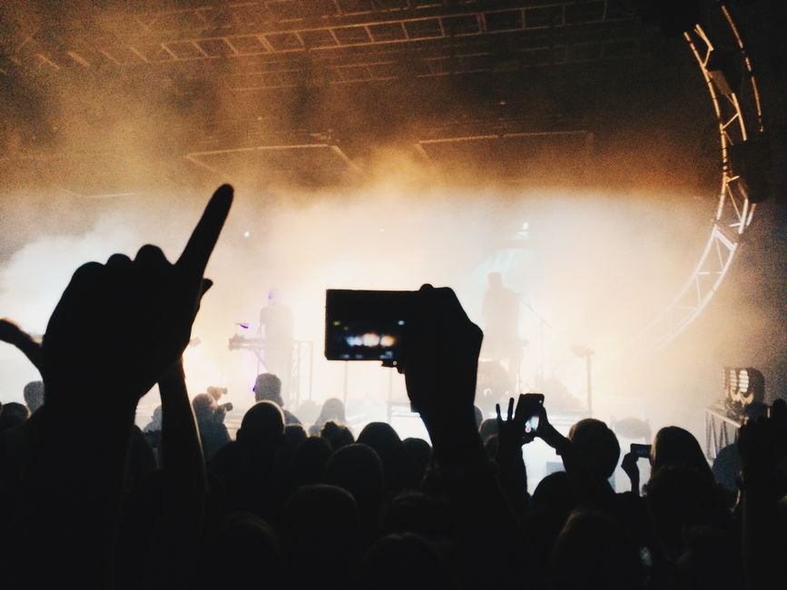 Silhouettes of a concert crowd filming with phones under stage lights, representing fans at a sold-out BTS stadium show