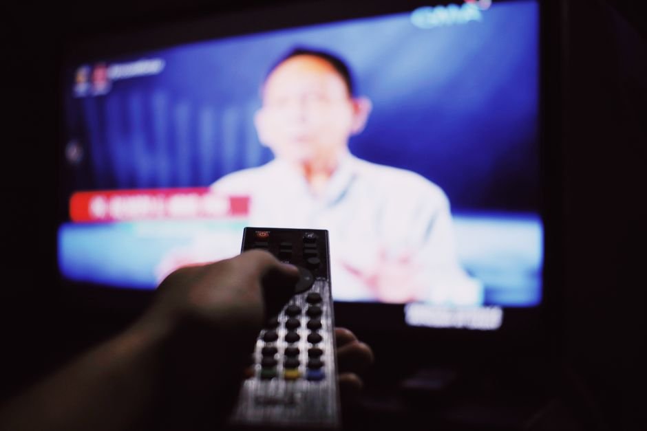 Person switching channels with a remote control in a dim living room, representing a streaming premiere night