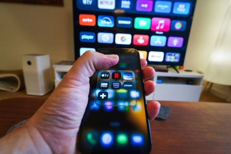 Hand holding a smartphone showing streaming app icons in front of a TV