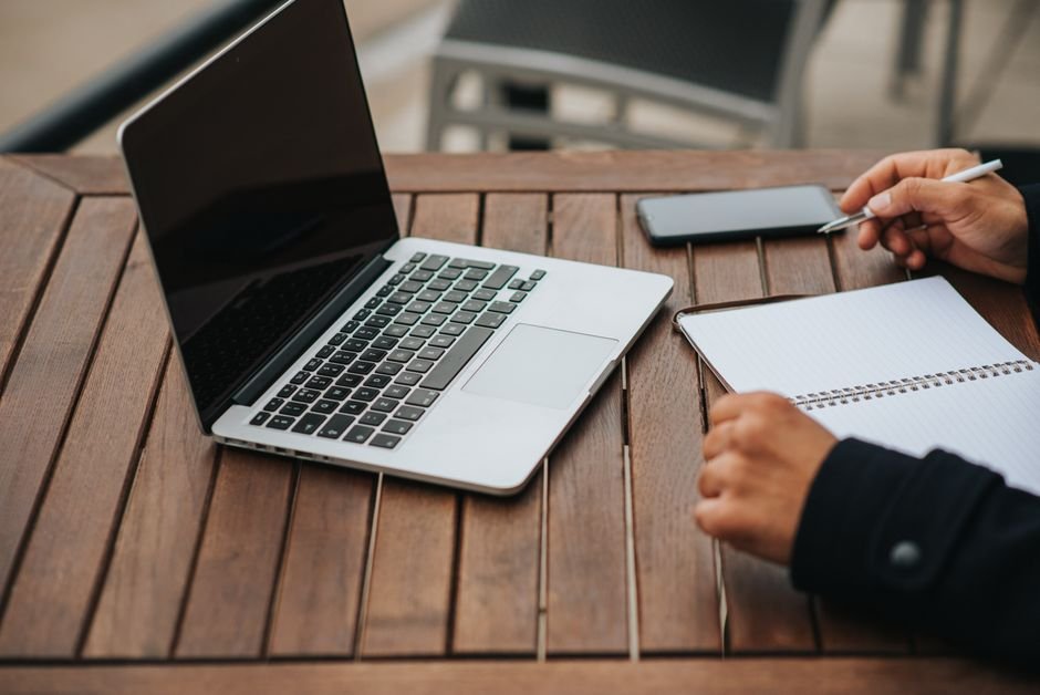 Freelancer working at a cafe table with a laptop and smartphone, representing an AI consulting side hustle