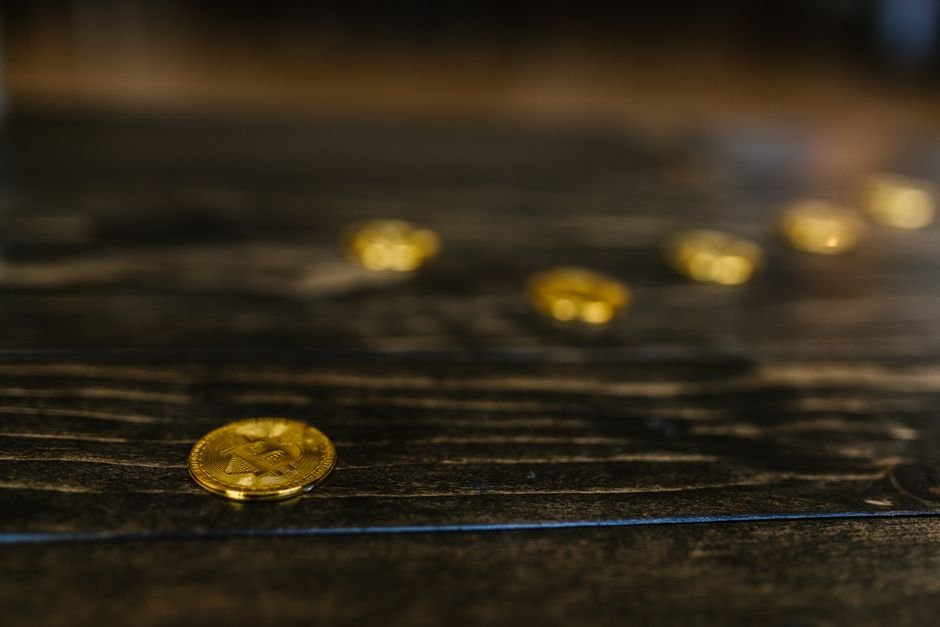 Gold Bitcoin coins on a wooden table, illustrating the cost of buying Bitcoin through a broker versus an exchange