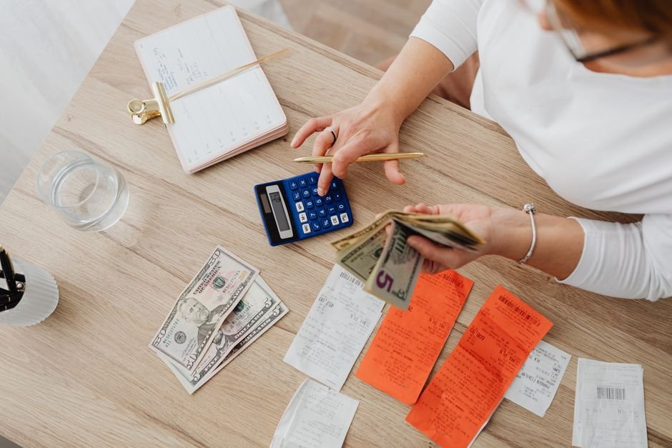 Person using a calculator with cash and receipts, working out card grading break-even math