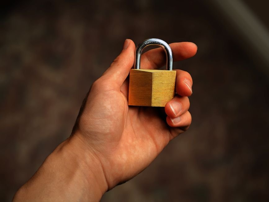 Hand holding a brass padlock, representing the trust decision before installing an unsandboxed Claude Code mod