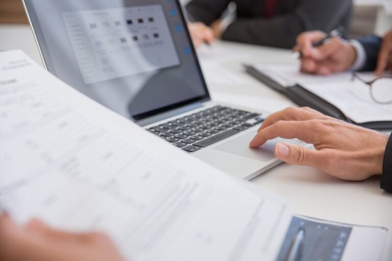 Hands working on documents next to a laptop, illustrating Claude for Google Workspace in Docs, Sheets, and Slides