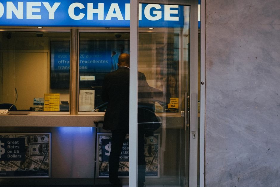 Man at a currency exchange window with rates displayed, illustrating foreign transaction costs on a crypto card