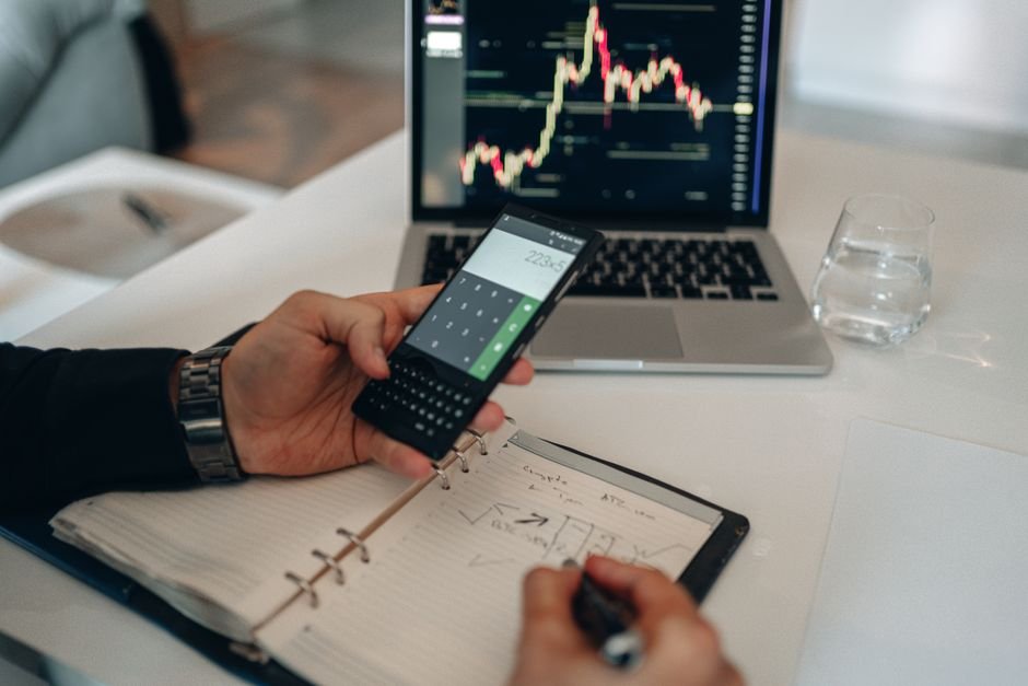 Person using a calculator and laptop with trading charts