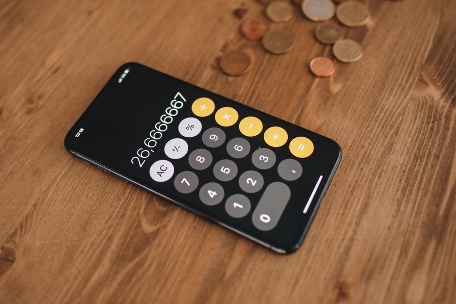 Smartphone calculator app surrounded by coins, used to work out the real cost of early pay fees