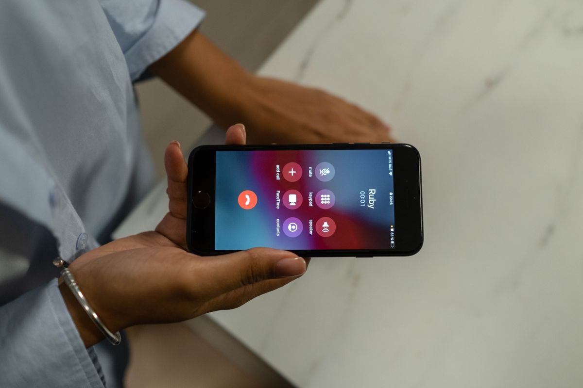 Hand holding a smartphone with an incoming call screen, for testing iPhone earpiece crackling on calls