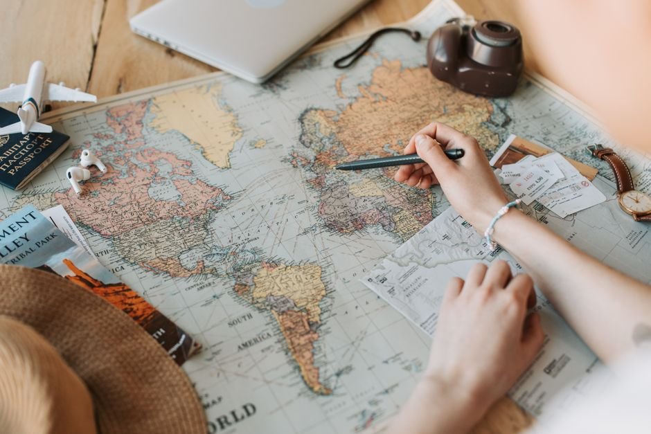 Hands marking destinations on a world map with passport and camera