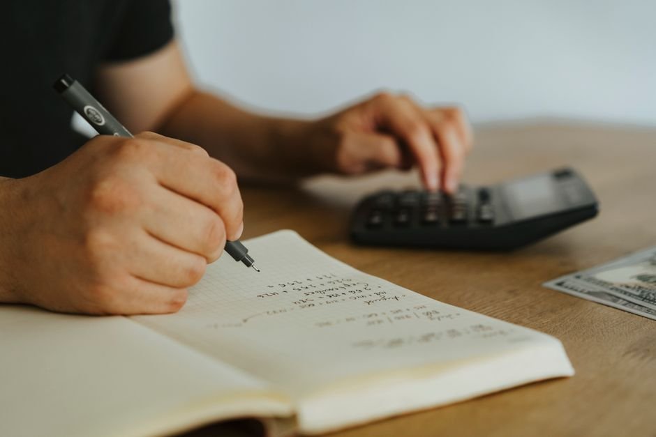 Hands writing margin calculations in a notebook next to a calculator