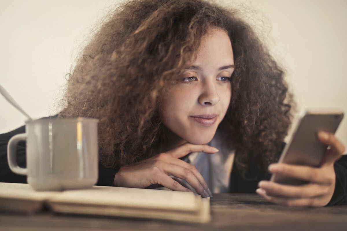 Person checking a smartphone notification while holding a coffee, deciding whether an email is legitimate