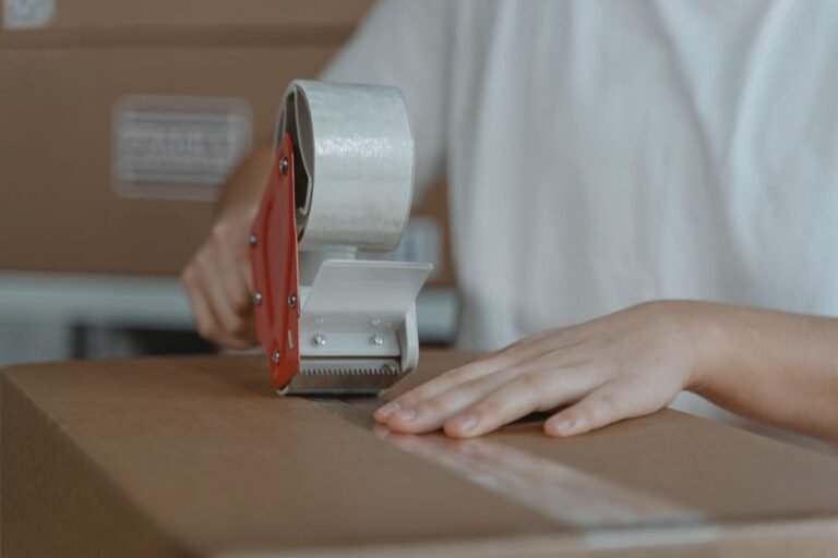 Seller taping a reused cardboard box, which should be checked for old HAZMAT markings before shipping