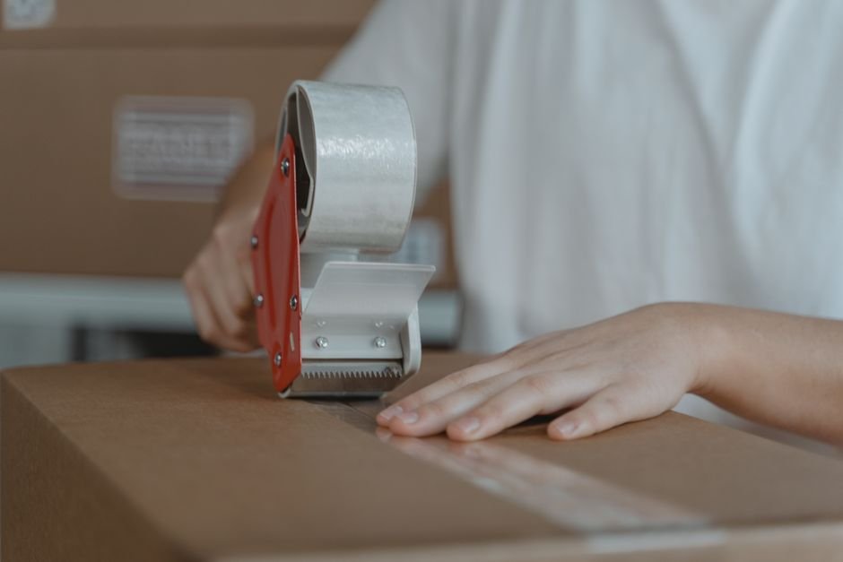 Seller taping a reused cardboard box, which should be checked for old HAZMAT markings before shipping