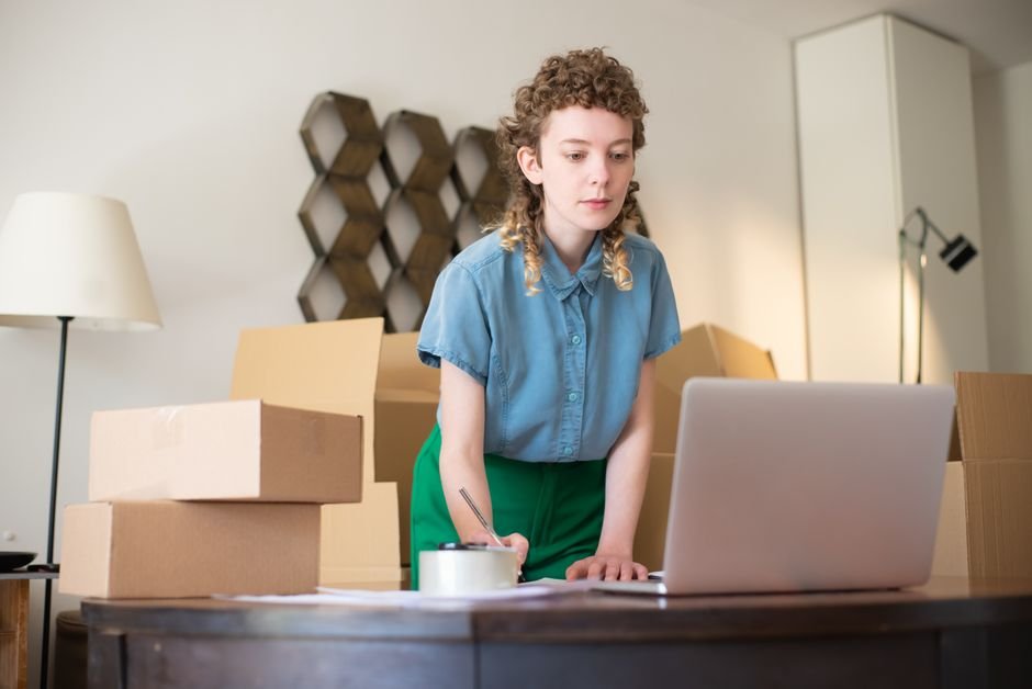 Online store owner working on a laptop surrounded by shipping boxes before canceling a Shopify subscription