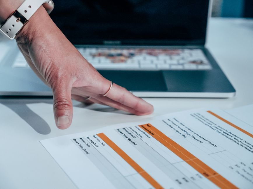 Hand reviewing a financial report on a laptop, checking marketplace fee invoices for Texas tax